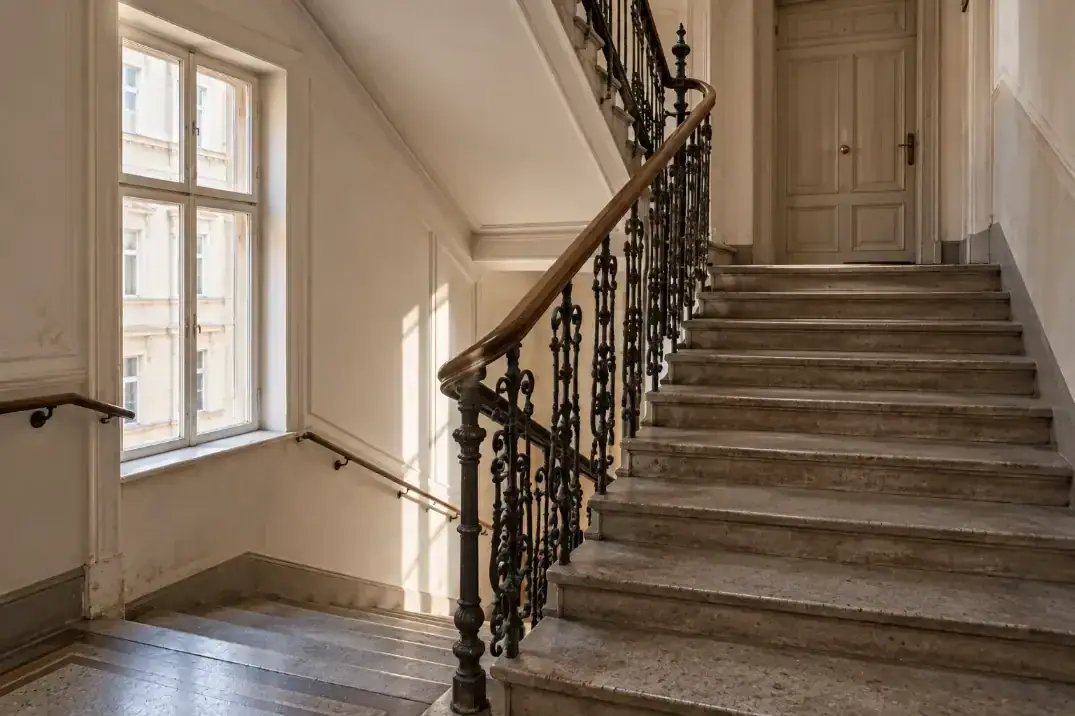 Leeres Wiener Stiegenhaus mit Steinstufen, schmiedeeisernem Geländer und Tageslicht vom Podestfenster